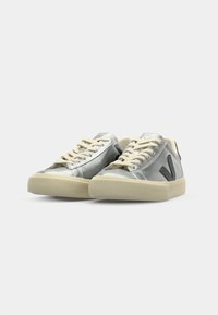 Sneaker sintetiche argentate con lacci crema, tomaia testurizzata e logo nero a contrasto sul lato. Suola in gomma, design low-top.