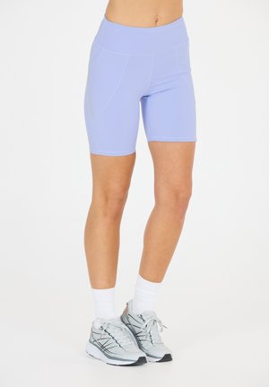 Lila sportshorts met een hoge tailleband, voorzien van zijzakken en een gladde textuur. Gecombineerd met grijze sneakers en witte crew-sokken.