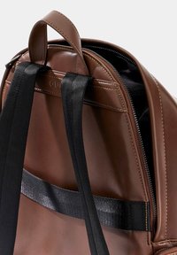Sac en cuir marron avec fermeture éclair, bretelles noires, finition texturée avec des coutures visibles et une poignée supérieure.