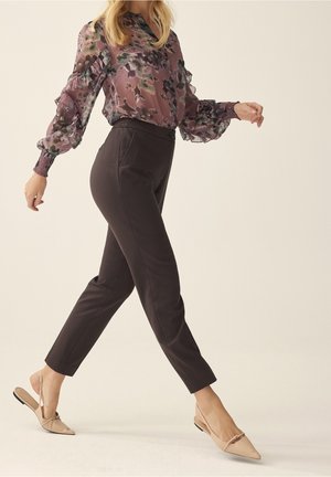 Välfutförd blommig blus i lila och gröna nyanser med volangdetaljer, kombinerad med figurnära svarta byxor. Spetsiga beige slip-on-skor.