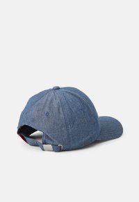 Blue denim-style cap with a curved brim, adjustable strap, and textured fabric. Back displays a small red accent and a silver hardware detail.