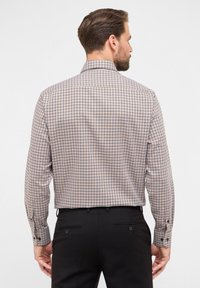 Camicia a quadri marrone, beige e blu navy, con maniche lunghe e colletto classico. Tessuto morbido con polsini abbottonati e vestibilità moderna.