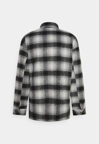 Flannel skjorte med et sort og hvidt plaidskema, lange ærmer og knapmanchetter. Stoffet ser struktureret ud med en blød overflade.
