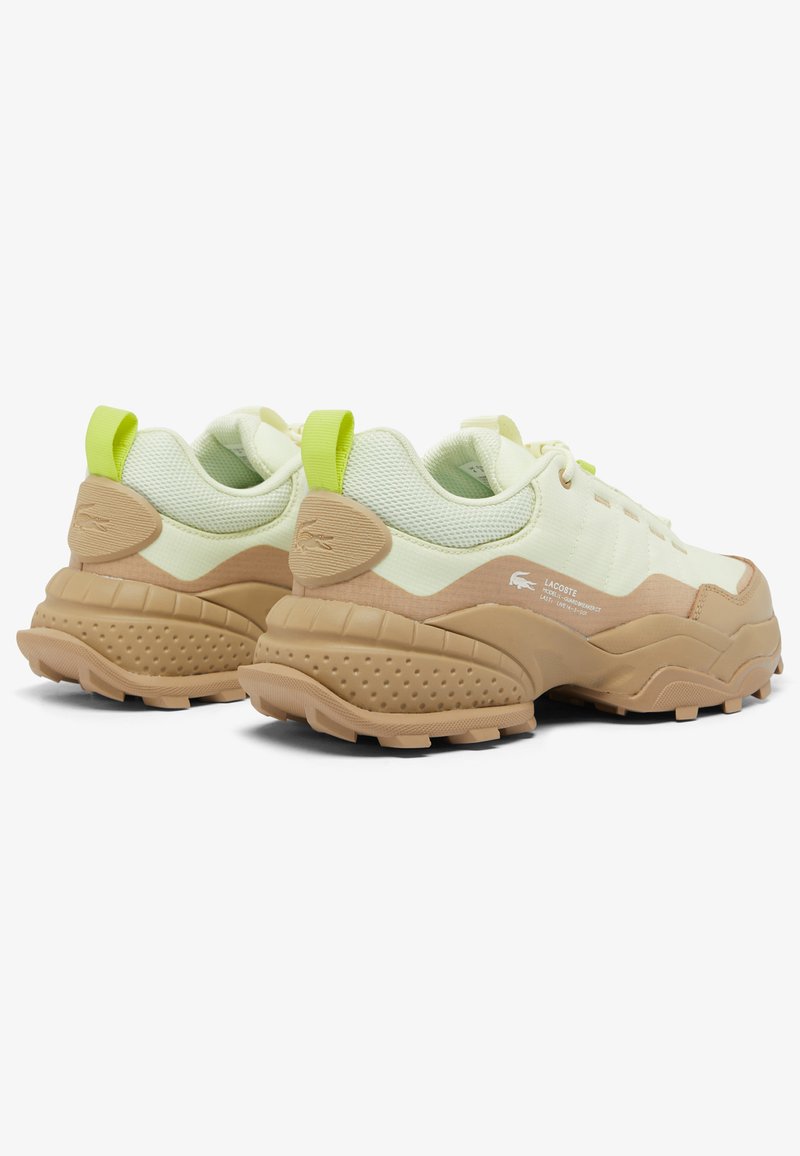 Sneaker Lacoste con una parte superiore in rete verde chiaro, accenti in gomma beige e una suola texture, dotata di linguette fluorescenti verdi sul tallone.