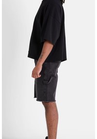 T-shirt nera oversize con maniche corte, abbinata a pantaloni corti in denim grigi con orlo sfrangiato e dettagli delle tasche laterali.