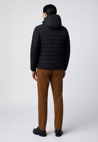 Giacca a vento nera con cappuccio, caratterizzata da sezioni trapuntate orizzontali. Abbinata a pantaloni marroni e scarpe nere.