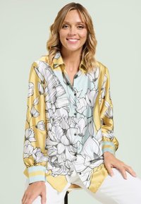 Silk blouse featuring a yellow and blue floral pattern, black buttons, and light blue cuff accents, with a relaxed fit and long sleeves.