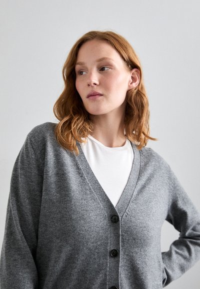 Grå cardigan med V-hals, lange ermer og fem svarte knapper foran. Myk stoff med en glatt tekstur.