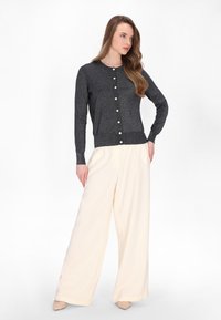 Donkergrijze button-up cardigan met een ronde halslijn, textuur gebreide stof en lichtkleurige knopen, gecombineerd met losse crème kleurige broek.