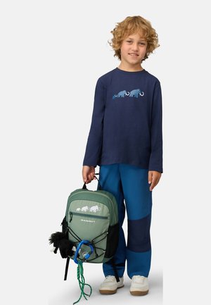 Groene rugzak met witte mammoetafbeelding, blauwe longsleeve met olifantenontwerp, blauwe en marineblauwe broek, witte sneakers, met een karabijnhaak.