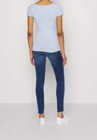 Camiseta de manga corta ajustada de color azul claro, combinada con jeans ajustados de color azul oscuro y zapatillas blancas. Diseño sencillo, textura de tela suave.