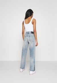 Jeans de mezclilla de lavado claro con cintura alta, pierna recta y ligero desgaste. Combinados con una camiseta sin mangas blanca y zapatillas blancas.