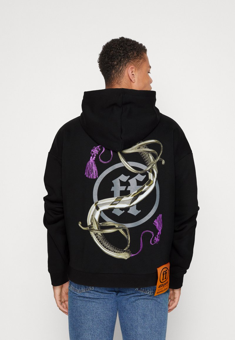 Svart hettegenser med et stort, grafisk design på baksiden med lilla detaljer, et sirkulært logo, og et stort oransje merke på siden.