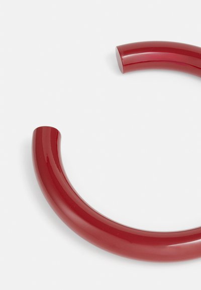 Mango de plástico rojo brillante, de forma curva, textura suave, diseño de bucle cerrado, extremos redondeados, con un color vívido constante en toda su extensión.