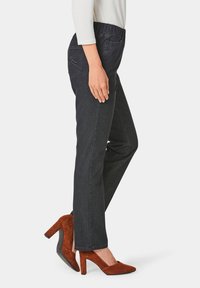 Pantalon en denim foncé avec une taille extensible, doté d'une poche latérale et de détails de couture subtils. Associé à des escarpins en suède marron.