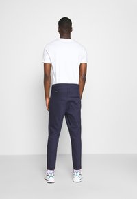 Pantalons ajustés bleu marine avec une texture lisse, coupe droite et une poche arrière. Associés à un T-shirt blanc uni et des baskets blanches.