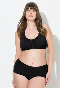 Conjunto de sujetador negro y braguitas de talle alto a juego. El sujetador cuenta con un cierre frontal y tela recogida. Material suave y elástico con bordes ondulados.