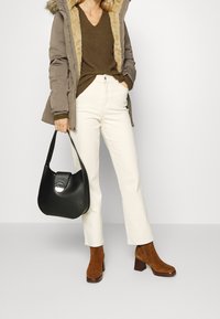 Bruna mockaskinnsankelboots, vita högmidjade byxor, olivgrön stickad tröja och en svart läderhandväska med ett runt lås. Pälsfodrad parkas.