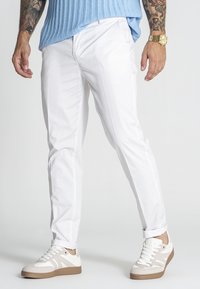 Weiße Slim-Fit-Hosen aus leichtem Stoff mit schlichtem Design und seitlichen Taschen, kombiniert mit weißen und beigen Sneakers.