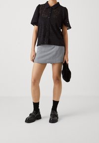 Svart spets kortärmad skjorta med krage, grå minikjol, svarta plattformsskor med nitar och en liten svart pälsclutch.