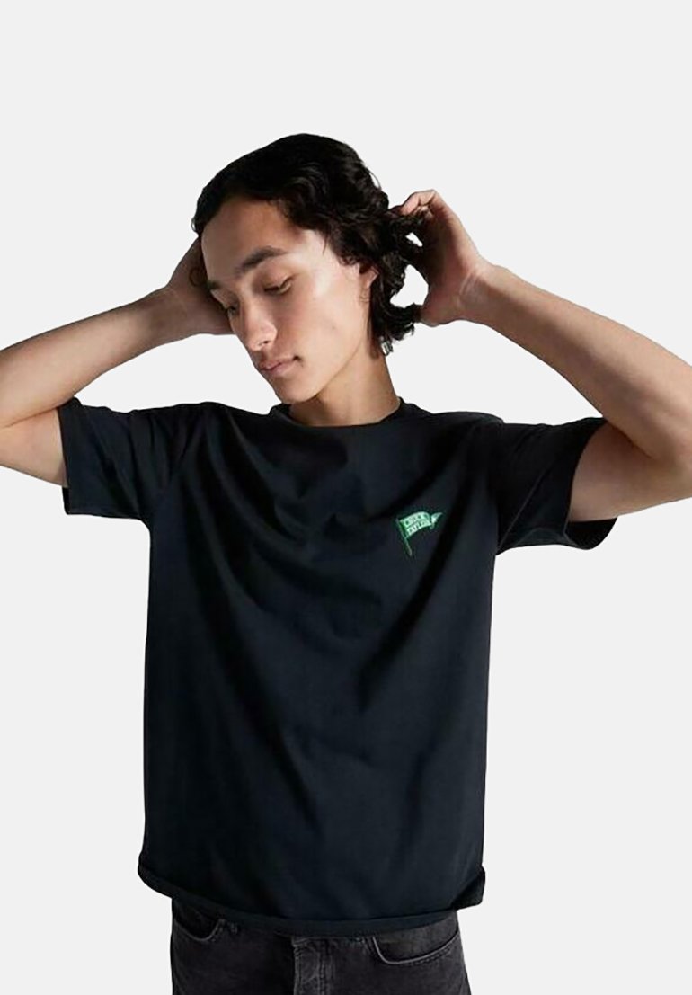 Camiseta de algodón negra con escote redondo y mangas cortas, que presenta un pequeño detalle gráfico en verde en el pecho. Corte relajado, textura suave.
