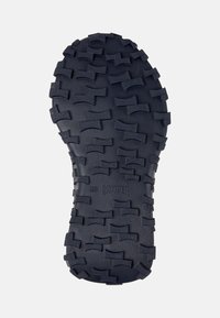 Suela de zapato de goma negra con un patrón texturizado que presenta diseños en zigzag y ondulados para tracción. Marcada con la impresión "CAMPER 28".