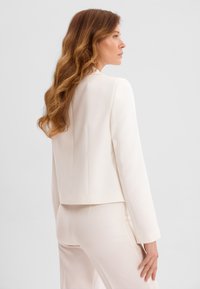 Bia�ła marynarka dopasowana, o wyraźnej linii, z wyraźnie zarysowanymi ramionami i długimi rękawami, w komplecie z dopasowanymi spodniami. Gładka faktura.