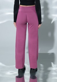 Hoge taille, wijde broek van ribbelstof in roze kleur. Kenmerkt zich door een stevige tailleband en een soepele textuur. Zwarte schoenen zijn zichtbaar onderaan.