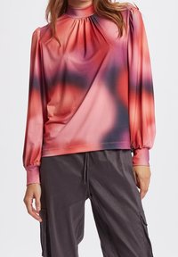 Långärmad topp i gradientnyanser av rosa och lila, med hög krage, samlad detaljer och elastiska ärmar. Slät textur.