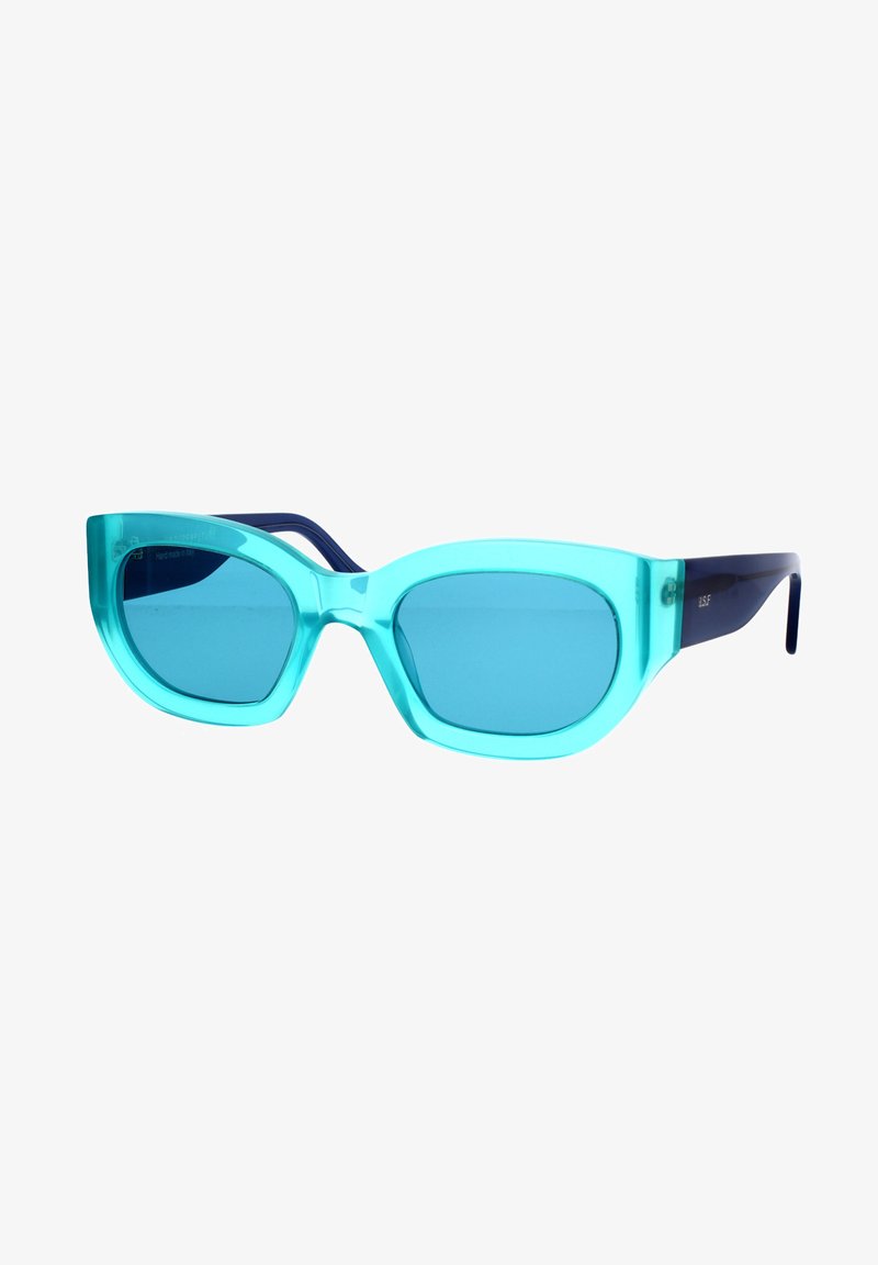 Un paio di occhiali da sole a occhio di gatto con montatura in acrilico traslucido color aqua e lenti blu. Le stecche sono di un blu navy scuro.