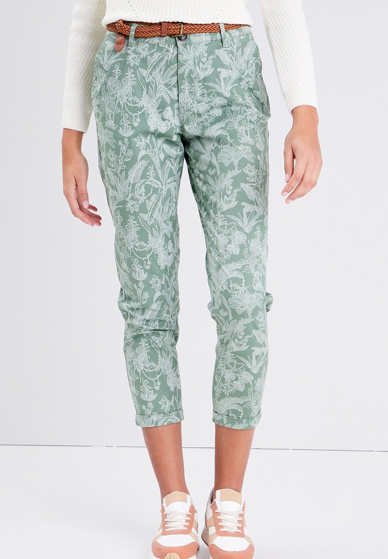 Pantalons à motif floral vert avec une coupe ajustée, ourlets retroussés et une texture lisse. Associés à des chaussures de sport blanches et pêche.