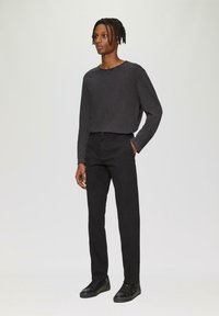 Zwarte longsleeve shirt met ronde hals, gecombineerd met zwarte rechte broek en zwarte sneakers. Soepele stof, minimalistisch ontwerp.