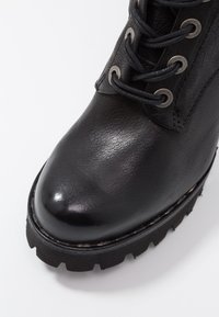 Stivale in pelle nera con punta rotonda, superficie texturizzata, occhielli metallici per i lacci e una suola nera spessa e robusta con un motivo a battistrada.