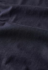 Navyblauwe stof met een gladde textuur, voorzien van fijne ribbels en een subtiele glans, die zacht valt met zichtbare plooien en kreukels.