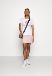 Biela tričko s ružovým logom "CONVERSE", svetloružová sukňa, čierna crossbody taška so vzorom leopardu, biele vysoké tenisky.