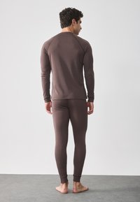 Barna hosszú ujjú felső és hozzáillő leggings puha, textúrált anyagból, bordázott mandzsettával és laza szabással. Hátulról látható.