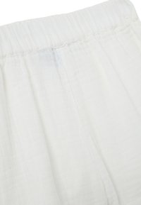 Witte katoenstof met een zachte, textuurrijke oppervlak, voorzien van een elastische tailleband en subtiele gatherdetails langs de bovenrand.