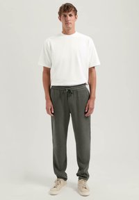 Hvit bomulls T-skjorte kombinert med olivengrønne bukser med elastisk midje og beige sneakers. antrekket har en avslappet passform og enkelt design.