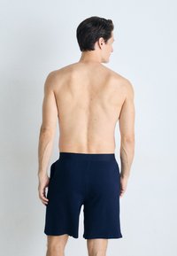Pantalones cortos deportivos de color azul marino con cintura elástica, que llegan hasta la mitad del muslo, mostrados desde la parte de atrás, revelando una tela suave y texturizada.