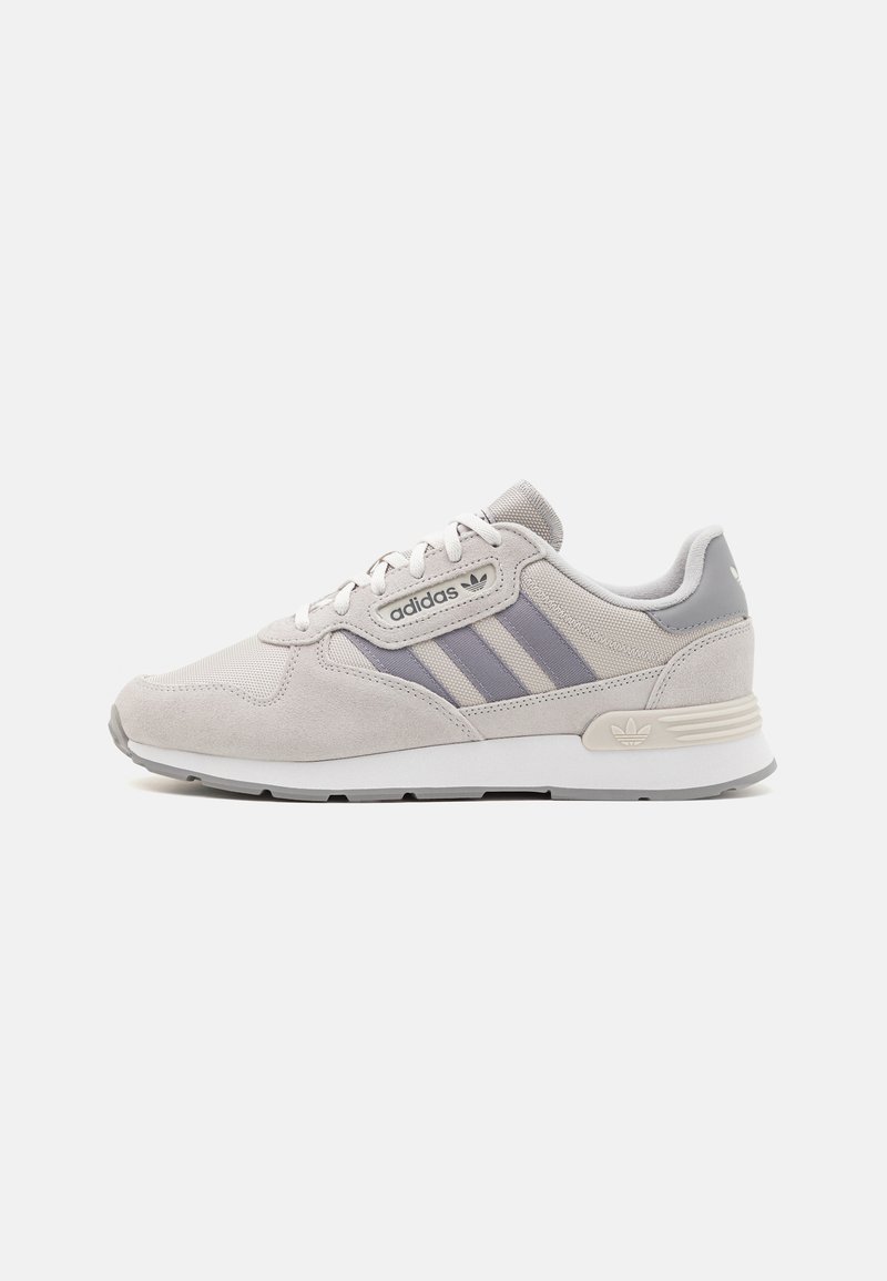 Graue Wildleder- und Mesh-Sportschuhe mit einer weißen Zwischensohle, die drei lila Streifen, runde Schnürsenkel und ein geprägtes Markenlogo aufweist.