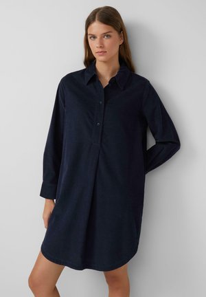 Hemdkleid aus dunkelblauem Cord mit langen Ärmeln, einer knöpfbaren Frontleiste und einem abgerundeten Saum, das einen klassischen Kragen und einen lässigen Schnitt aufweist.