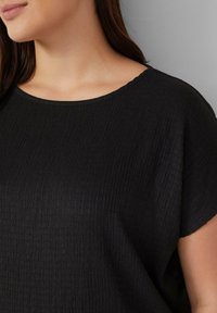 Zwarte top met een ronde halslijn en korte mouwen, gemaakt van een textuur-achtige, crepe-achtige stof voor een relaxte pasvorm. Eenvoudig en veelzijdig ontwerp.