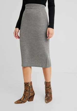 Femme portant une jupe midi en maille côtelée grise, un haut noir à manches longues et des bottines marron en cuir de serpent avec talons blocs.