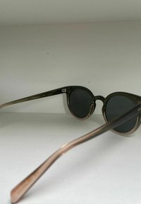 Lunettes de soleil rondes avec des montures vertes et des verres foncés. Les branches présentent un dégradé allant du vert foncé au rose doré, avec des détails de marque.