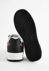 Schwarze Ledersneaker mit weißer Sohle, grauem Futter und roten Akzenten hinten; strukturierte schwarze Gummisohle mit einem Profil.