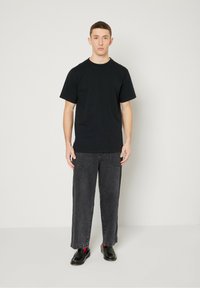 Black cotton T-shirt, short sleeves, round neckline; paired with dark gray wide-leg denim pants. Black leather shoes with red sock accents.