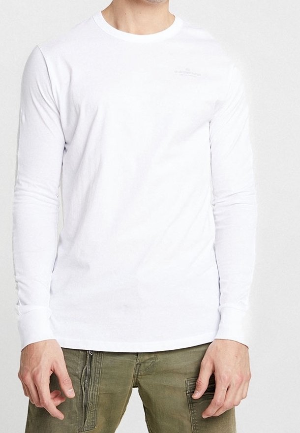 Vit långärmad t-shirt i bomull, med rund halsringning och subtil branding på bröstet. Slät textur med tighta ärmar.