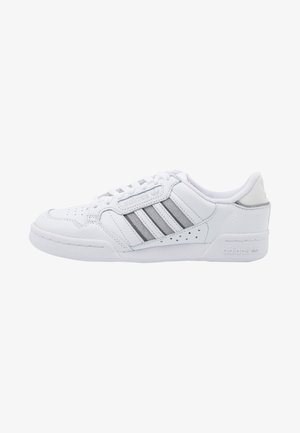 Zapatilla baja blanca de Adidas con rayas grises, puntera perforada, cuello acolchado y suela y lateral con marca.