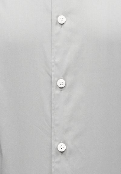 Κοντινή λήψη τριών λευκών κουμπιών ραμμένων σε ένα γκρι ανοιχτό πουκάμισο με ορατή ραφή κατά μήκος του ποδόγυρου με τα κουμπιά.