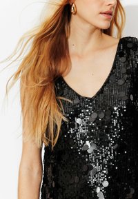 Haut noir à sequins avec un décolleté en V profond, orné de sequins circulaires brillants et de tissu texturé. Un look lisse et élégant.